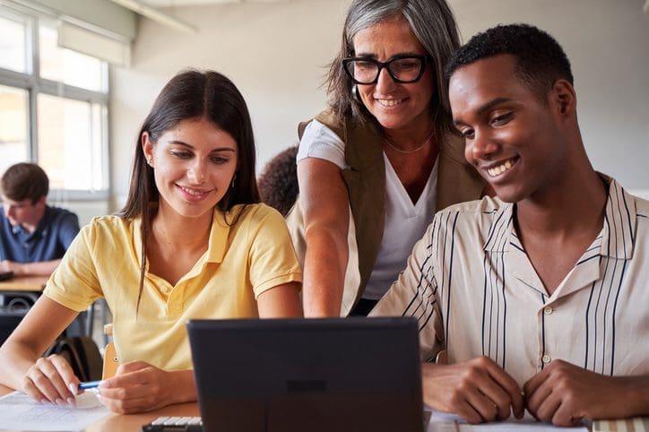 Three people collaborating and smiling around a laptop.