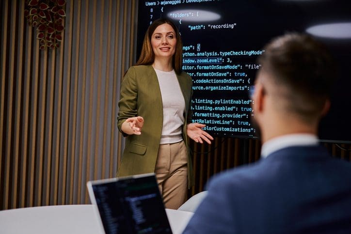 A woman giving a tech presentation to a colleague in an office.